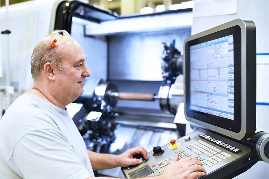 Facharbeiter in der Industrie bedient eine CNC Drehmaschine zur mechanischen Bearbeitung im Maschinenbau