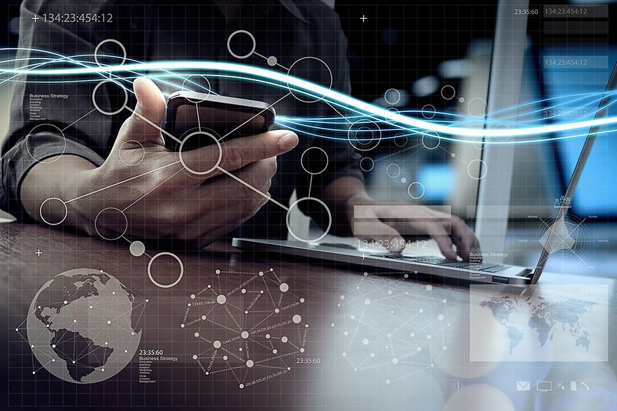 Mann bedient mit einer Hand seinen Laptop und mit der anderen Hand sein Smartphone