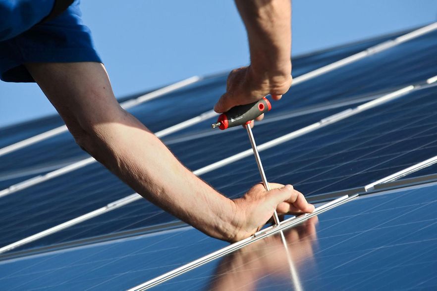 Jemand schraubt eine Solaranlage auf einem Dach fest.