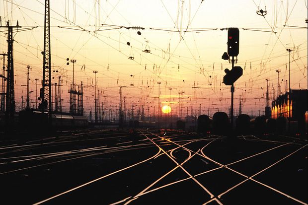 Bahnhofsvorfeld mit Gleisen und Oberleitungen bei Sonnenuntergang oder Sonnenaufgang.