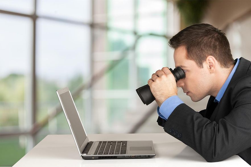 Mann mit Fernglas vor Laptop