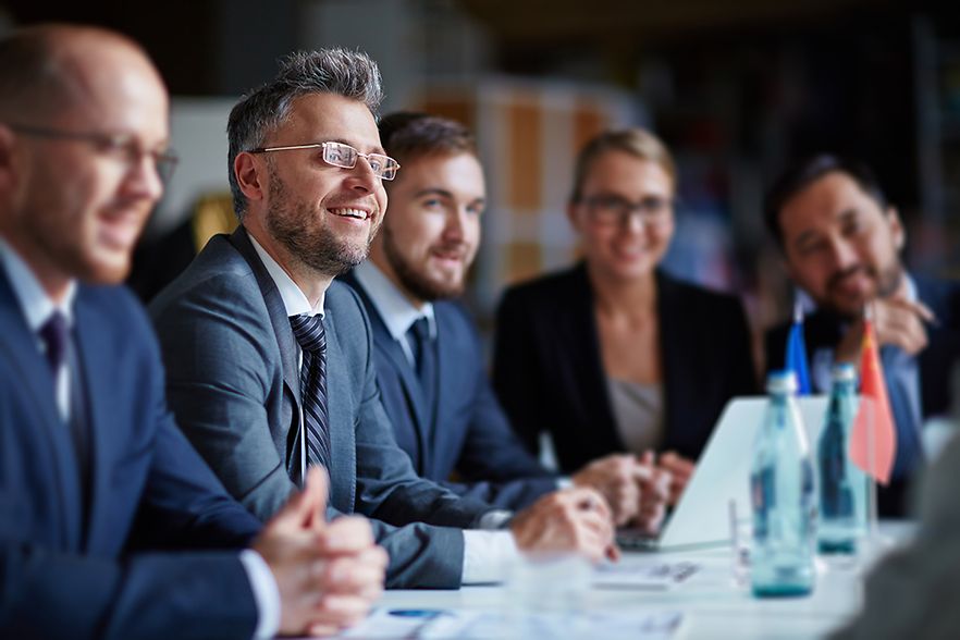 L&auml;chelnde Gesch&auml;ftsleute sitzen in einer Tischreihe eines Seminarraums