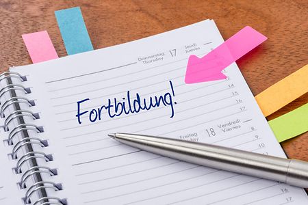 Zu sehen ist ein Kalender mit mehreren Post-its und einem Kugelschreiber. Ein Tag wurde mit Fortbildung markiert.