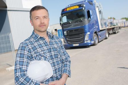 Ein Mann mit Helm unter dem Arm steht vor einem Lkw