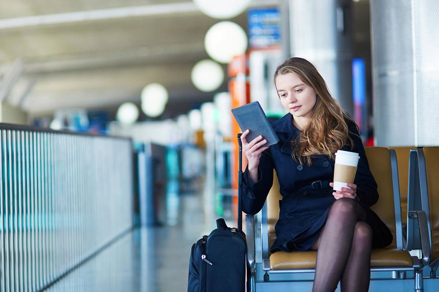 Eine junge Frau liest, w&auml;hrend sie am Flughafen wartet und Kaffee trinkt.