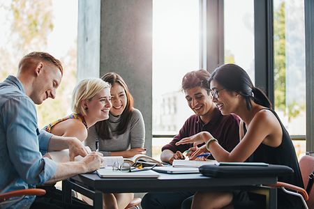 eine Gruppe lachender Studenten sitzt in der Biblithek an einem Tisch