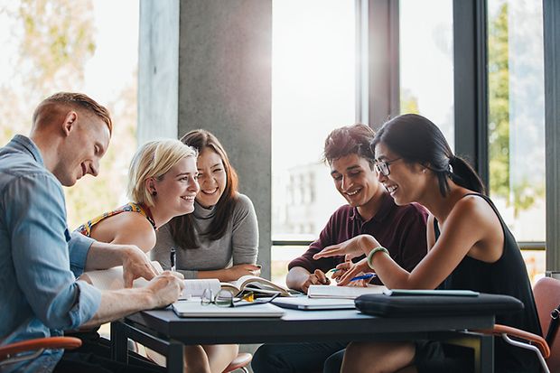 eine Gruppe lachender Studenten sitzt in der Biblithek an einem Tisch