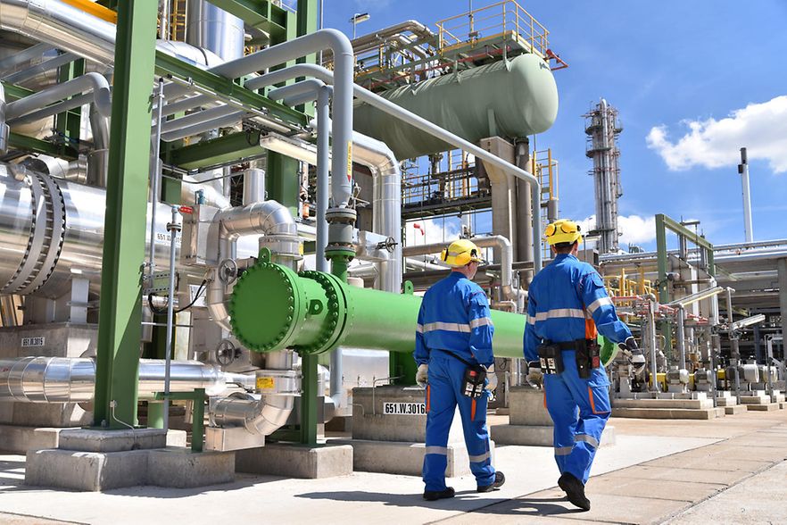 Arbeiter laufen an einer Chemieanlage entlang