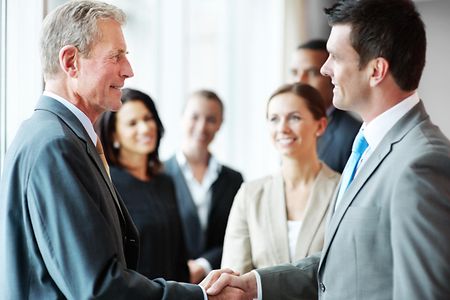 Two business men shaking hands with their teams in background