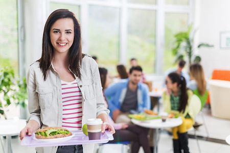 Student holding a tray in cafeteria and looking at camera.