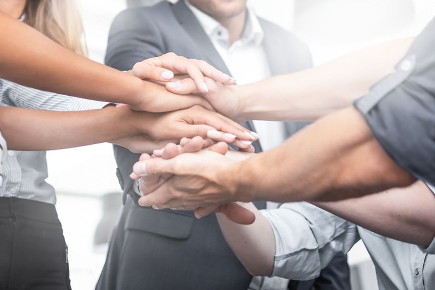 F&uuml;nf Menschen stehen im Kreis und legen H&auml;nde aufeinander
