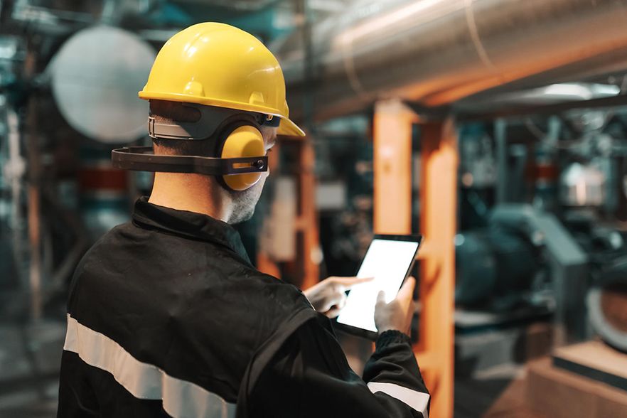 R&uuml;ckansicht eines Arbeiters mit gelbem Helm und Tablett in einem Gaskraftwerk