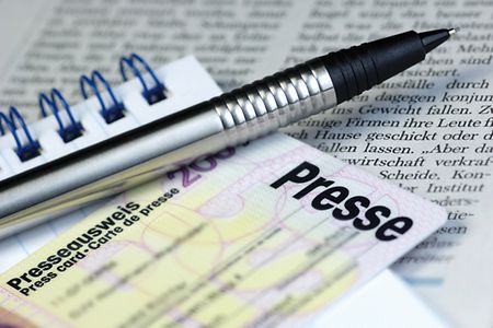 Kugelschreiber und Presseausweis liegen auf Notizblock und Tageszeitung. 