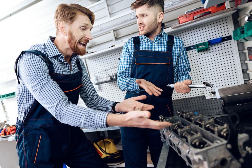 M&auml;nner in blauen Overalls streiten in der Autowerkstatt
