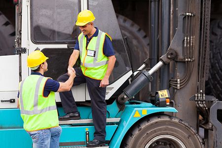 Arbeiter mit Warnwesten und Helmen reichen sich die H&auml;nde