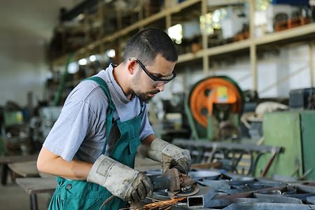 junger Migrant in der Fabrik bei der Arbeit an einer Maschine