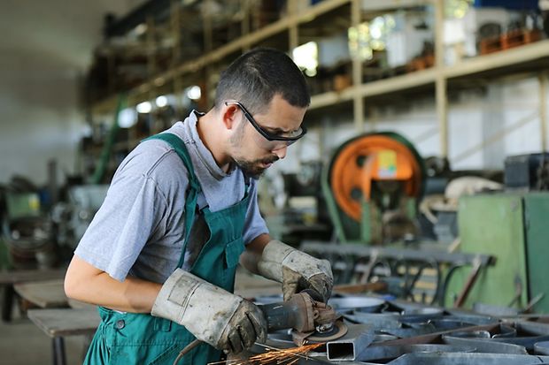 junger Migrant in der Fabrik bei der Arbeit an einer Maschine