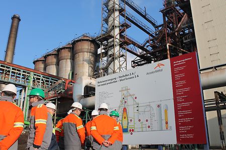Gruppe von Menschen steht vor Hochofen zur Roheisenerzeugung 