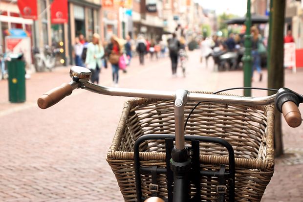 Ein Fahrrad mit einem Einkaufskorb am Lenker steht in einer Fu&szlig;g&auml;ngerzone mit Passanten