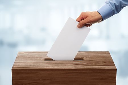 Hand steckt einen Briefumschlag in Wahlurne
