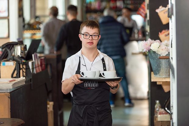 Junger Mann mit Down-Syndrom als Servicekraft in einem Cafe