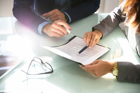 Vier H&auml;nde mit Kugelschreibern und einem bedruckten Papier