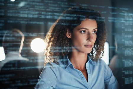 Digitally enhanced shot of an attractive businesswoman working in the office superimposed over multiple lines of computer code