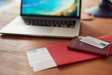 Laptop mit Strandhintergrund, Reisepass und Flugticket liegen davor
