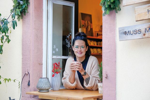 Denise Pitzer schaut aus dem Fenster Ihres Caf&eacute;s mit Tasse in der Hand