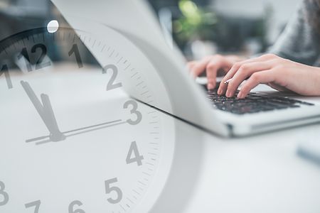 H&auml;nde tippen auf Laptop, Uhr im Vordergrund