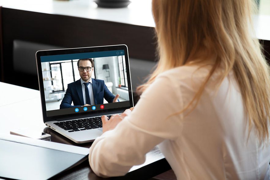 Eine Frau schaut auf einen Laptop-Bildschirm, auf dem ein Mann im Anzug zu sehen ist.