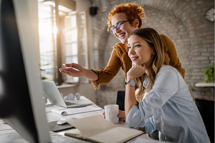 Young happy businesswomen cooperating while using desktop PC in the office. 