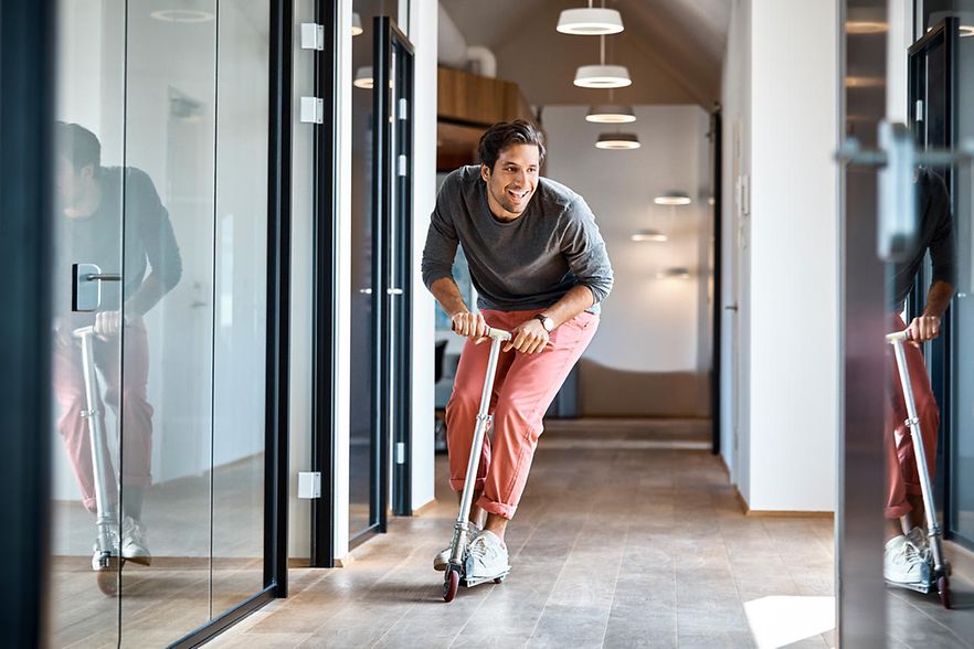 Mann f&auml;hrt mit einem Roller durch den B&uuml;roflur