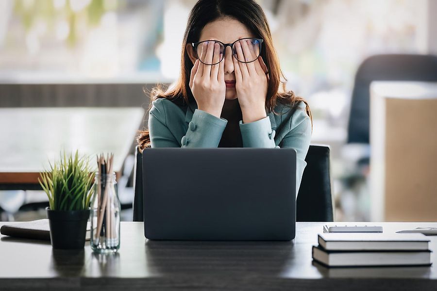 Eine Frau sitzt am Laptop. Sie hat die Brille hochgeschoben und reibt sich die Augen mit der flachen Hand.