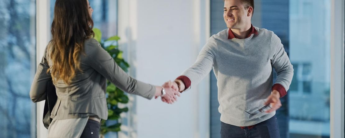 Dekoratives Bild: zwei Menschen begr&uuml;&szlig;en sich mit Handschlag an einem Schreibtisch