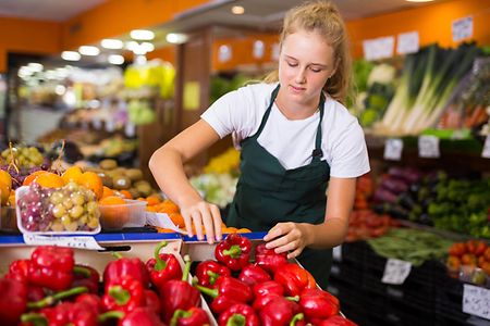 Young female seller holding pepper in grocery