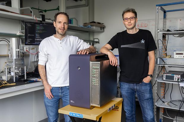 Zwei M&auml;nner stehen neben einem Photonendetektor.