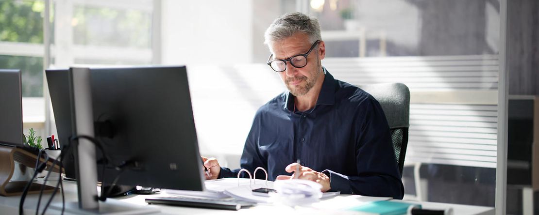 Dekoratives Bild: Person sitzt am Schreibtisch vor einem PC.