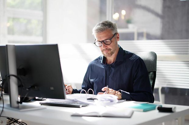 Dekoratives Bild: Person sitzt am Schreibtisch vor einem PC.