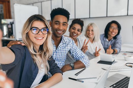 Mehrere junge Menschen sitzen zusammen an einem Schreibtisch und schauen in die Kamera