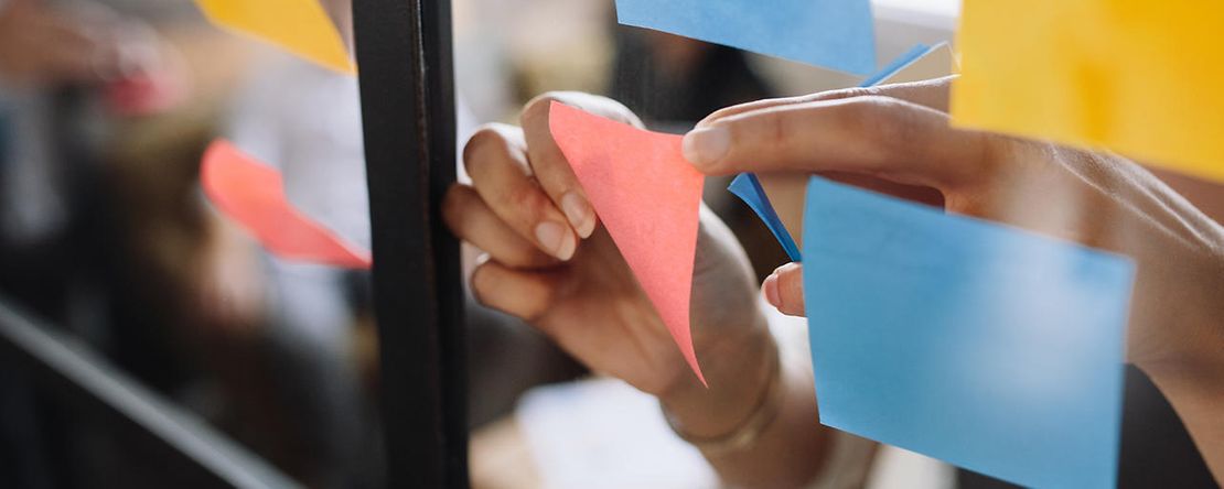Bunte Post-its kleben an einer Fensterscheibe.