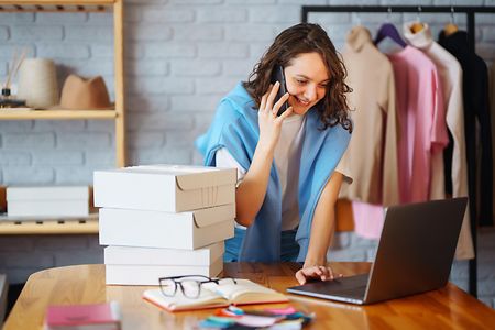 Frau mit Handy und Laptop in einem Bekleidungsladen