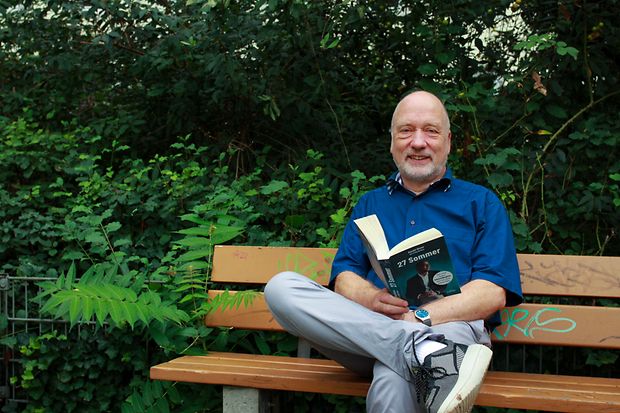 Ulrich Holl mit einem Buch auf einer Bank im Park