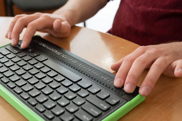 Ein Blinder benutzt einen Computer mit Braillezeile und Computertastatur
