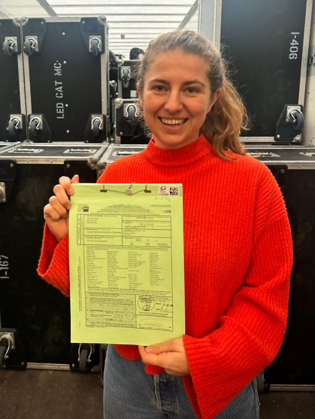 Maike Todeskino steht vor den Koffern mit Equipment und hält das Carnet hoch. 