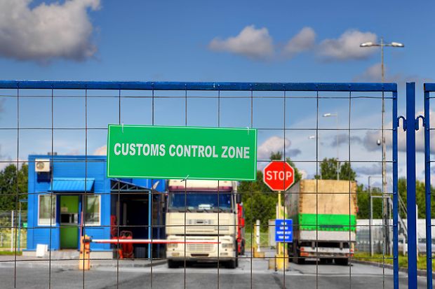 Hinter einem Zaun mit dem Schild &bdquo;Zoll&ldquo; sieht man ein paar Lkw an der Grenze stehen. 