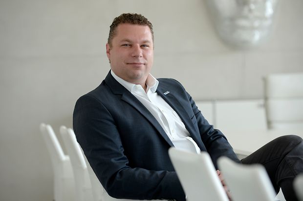 Stephan Kulbatzki sitzt im Anzug auf einem wei&szlig;en Sessel 