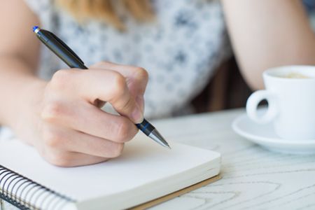 Hand, die Kugelschreiber h&auml;lt und etwas in ein Notizbuch schreiben m&ouml;chte