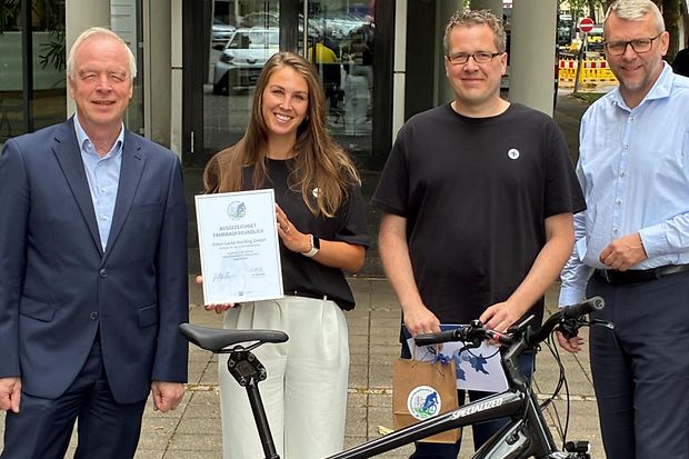 Vier Personen mit Fahrrad vor der IHK in Bielefeld bei der &Uuml;bergabe des IHK-Siegels "Ausgezeichnet Fahrradfreundlich".