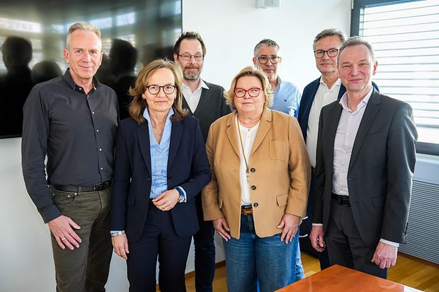 Gruppe von sieben Personen in Businesskleidung steht zusammen und blickt in die Kamera.